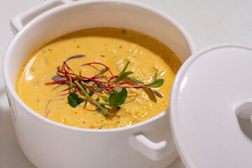 Pumpkin cream soup served with herbs in ceramic pot with lid