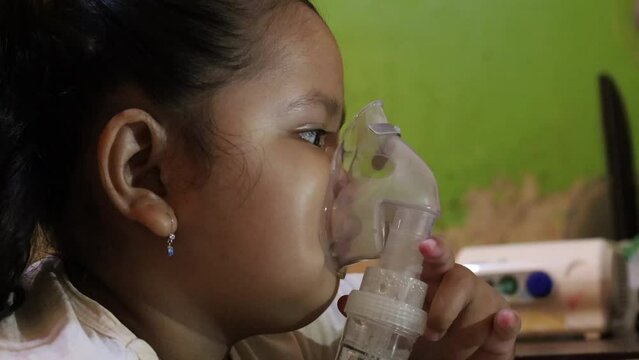 Asian Little girl making inhalation with nebulizer at home. Child asthma inhaler inhalation nebulizer steam sick cough concept