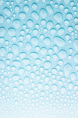 Water droplets on soft light aqua blue background as fresh cold color pattern, texture of shine different form drops with gradient, top view, vertical.