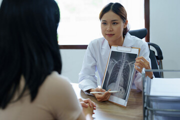 An Asian female doctor points to a patient x-ray film to explain the patient's treatment process