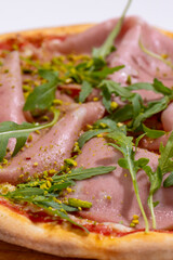Pizza with ham, arugula and pistachios served on wooden platter