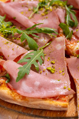 Pizza with ham, arugula and pistachios served on wooden platter