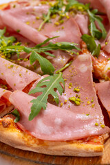 Pizza with ham, arugula and pistachios served on wooden platter