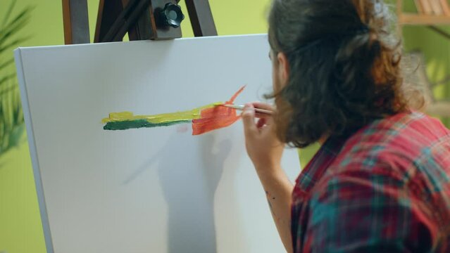 A close up of a handsome painter with a manbun using many colours to paint on his new canvas