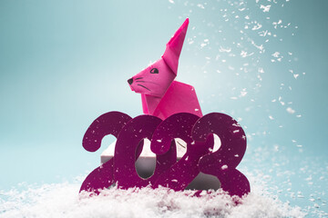 Blue background with the numbers 2023, pink rabbit and snow flakes close-up
