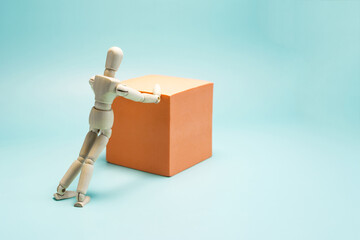 The concept of effort and overcoming. A wooden figure of a man is trying to move a cube of bright orange color.