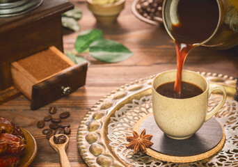 Pouring turkish  coffee into cup. 
 Cup of coffee placed with roasted coffee beans, fresh dates and ground coffee on rustic wooden background.