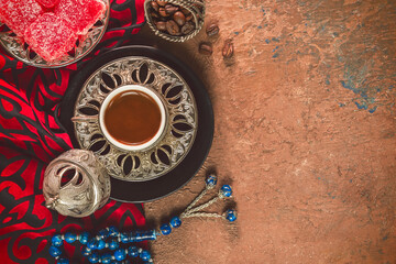 Turkish coffee cup placed with roasted coffee beans, Turkish delights and rosary beads on rustic background. Top view with copy space.