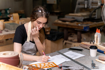 Portrait of a female carpenter drawing on paper for designing and building furniture in a furniture factory. with modern tools