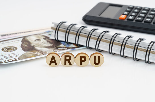 On a white surface are dollars, a notebook, a calculator and wooden circles with the inscription - ARPU