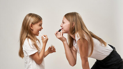 Side of teenage and little girls painting lips