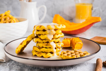 A stack of Belgian homemade pumpkin waffles topped with sweet sauce on a plate on the table