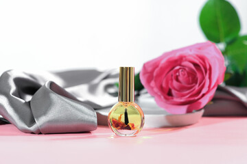 cuticle massage oil with rose petals infusion. pink rose flower next to a bottle of nail care oil, hans and nails beauty care, skin moisturizing and nourishing, spa manicure concept.