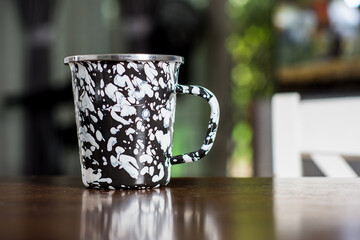 Black and white patterned old metal mug or enamel cup on a wooden table on blur background