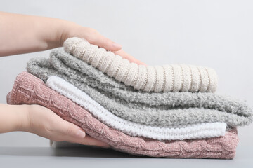 female hands holding a pile pastel color jumpers and other knitted clothing. winter apparel, trendy pale textured knitwear. cozy fall pullovers.
