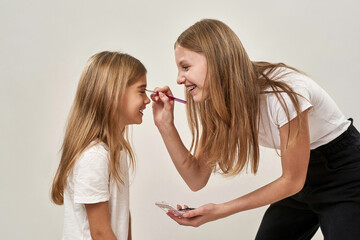 Girl painting glitter eyelid of sister on white