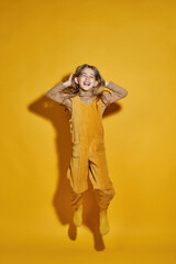 Excited little girl jumping on yellow background