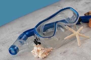 Blue snorkel mask with shells on the sand and blue background