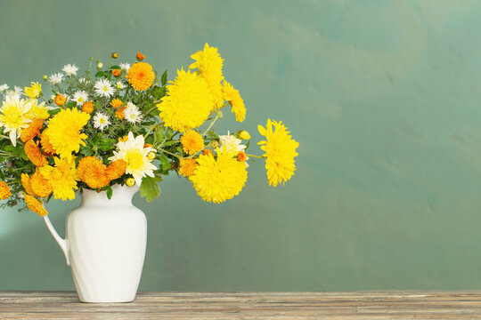 yellow and white chrysanthemum in white jug on wooden table