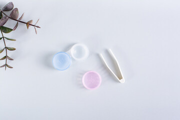 An open container with contact lenses and tweezers on a blue background. Top view.