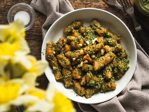 Close-up of a plate with homemade vegan pumpkin gnocchi in wild garlic pesto sauce, top view, served on a rustic wooden table with yellow flowers in the corner