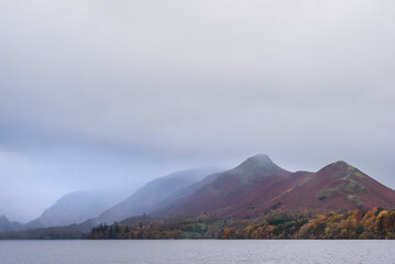 Stunning landscape image of Catbells viewed acros Derwentwater during Autumn in Lake District with mist rolling across the hills and woodland