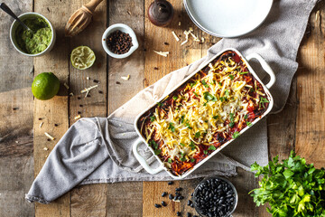 Vegan enchilada, a Mexican dish with sweet potato, tortilla, corn, tomato salsa, and black beans on a wooden rustic table with served dish in a plate with guacamole dip and a chair in back 