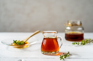 Thyme honey in small jug and jar, small thyme branch on white wooden table with grey background