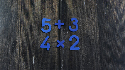 Task in mathematics. Mathematics problem for children. Simple algebra examples using numbers and signs from plastic numbers on a wooden background.