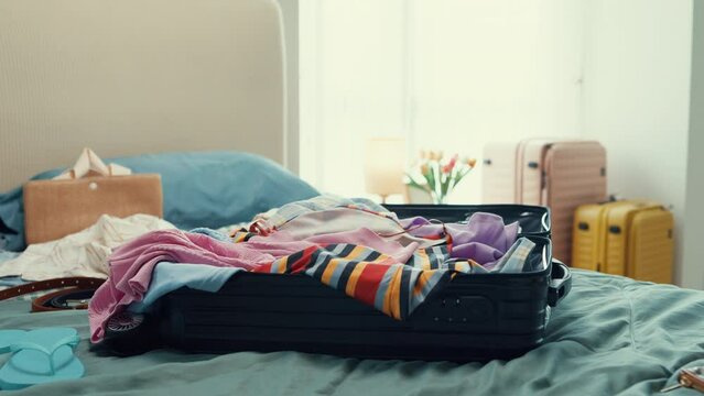 Young happy and exciting Asian female ready for summer holidays prepare suitcase throw cloth accessories messy stuff in bag in bedroom. Preparing luggage for summer vacation trip. Travel concept.