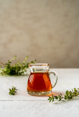 Thyme honey in small jug, fresh thyme on white wooden table with grey background