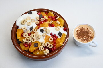 Fondo con textura y detalle de bol de macedonia con yogur y cereales, junto a un café con cacao