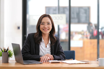 Portrait of smiling beautiful business asian woman with working in modern office desk using laptop...