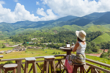 Fototapeta na wymiar back view of woman wearing white tank top and hat sitting on wooden chair seeing the nature foogy over mountain,travel concept
