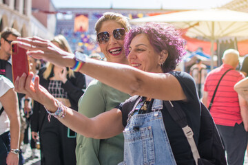 Happy mature friends taking a photo.
Cheerful mature friends laughing in casual clothes at a street gift market take a selfie photo on cell phone in the crowd.