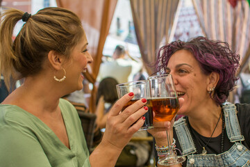 Cheerful Mature Friends In Casual Clothes Sitting At A Table With A Glass  Toasting And Laughing On A Restaurant Terrace. Lifestyle