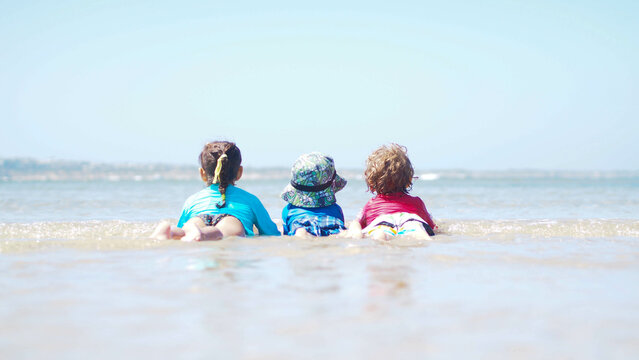 Three kids lying in the surf at the beach