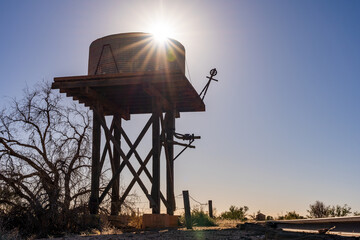 Silhouette of a high tank stand with an old water tank on top and the Sun peaking out from behind