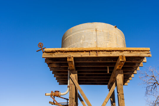 Looking up underneath a high tank stand with a rusting water tank on top and blue sky behind