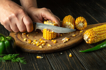The chef cuts corn kernels with a knife. Maize is an excellent dietary breakfast or lunch by the cook hands. Space for recipe or menu.