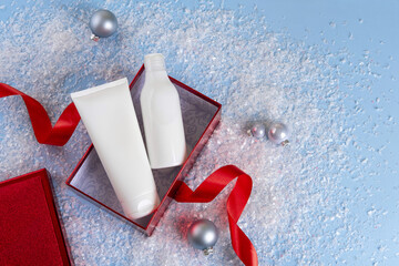 White bottles cosmetic products in red giftbox and on on a snowy blue background. Christmas sale of beauty products concept. Top view with place for text. Christmas promo.