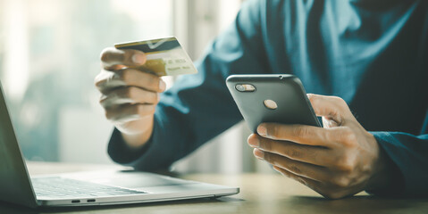 Man holding credit card and using smartphone at home online shopping ecommerce internet banking spend money work from home concept.