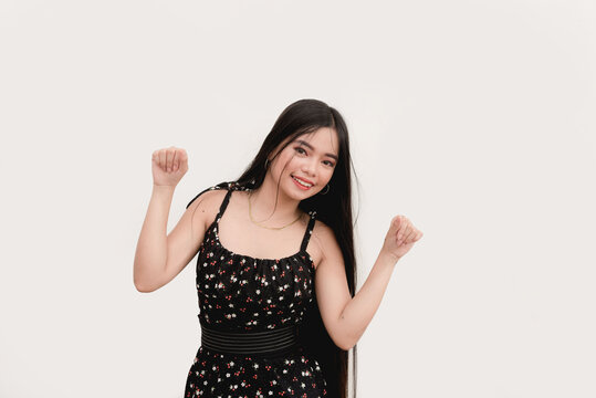 A pretty girl with long black hair wearing a floral dress dances to the music while smiling for the camera for a studio shot isolated on a white background.
