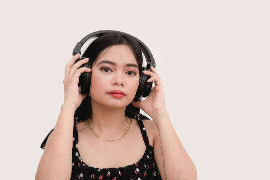 An Asian woman with a blank expression listens to a song with her bluetooth headset. Studio shot isolated in a white background.