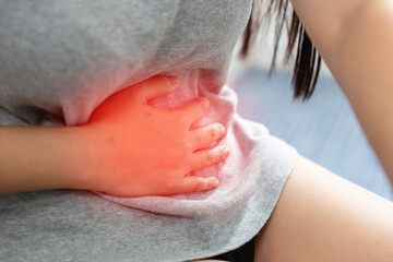 Fototapeta premium woman hand touching abdomen having stomach ache, female eating food poisoning causes flatulence, digestive disease, Abdominal pain during menstruation.