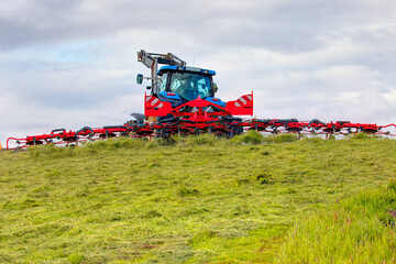 Modern tractor on wheat field near green trees