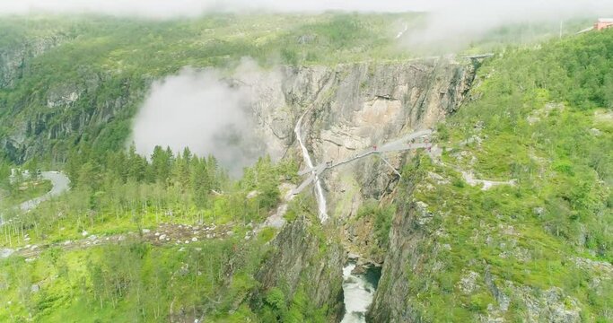 People walking on steel bridge crossing over V&oslash;ringsfossen canyon; drone