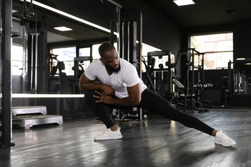 Muscular african man at the gym doing stretching exercises on the floor.