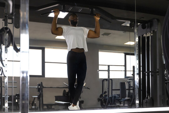 Fit and muscular african man pulling up on horizontal bar in a gym.