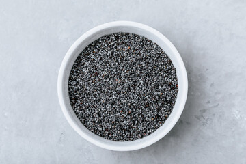 Fototapeta na wymiar Poppy Seeds.Dry raw poppy seeds in bowl on gray stone background. Top view, copy space.